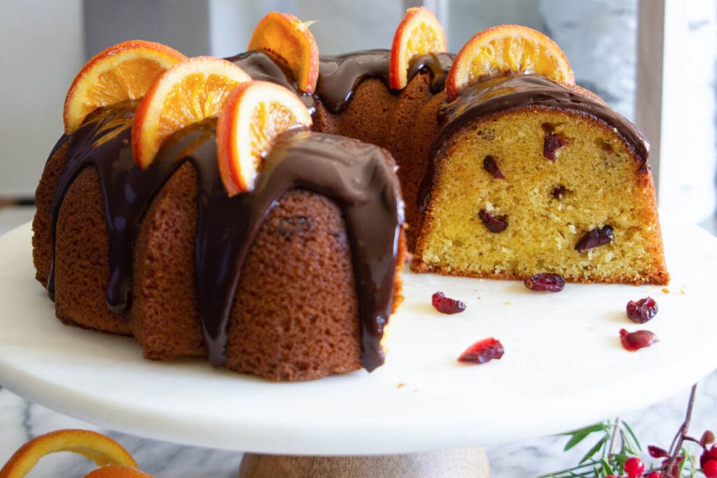क्रैनबेरी ऑरेंज बंडट केक के ऊपर संतरे के स्लाइस और गैनाचे डालें और काटें।