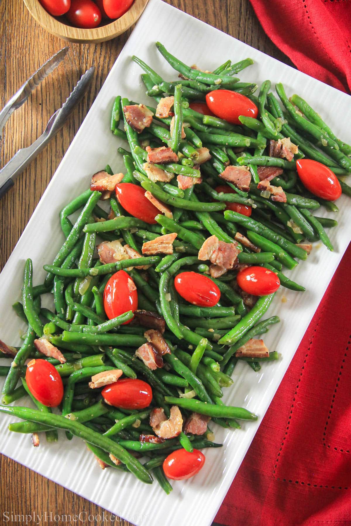 Green Bean Salad with Bacon on a white plate with tongs. 
