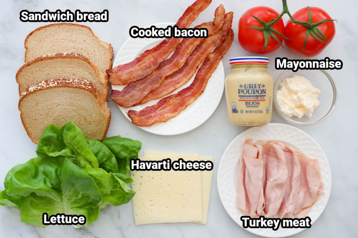 टर्की क्लब सैंडविच के लिए सामग्री: सैंडविच ब्रेड, पका हुआ बेकन, सलाद, टमाटर, डिजॉन सरसों, मेयोनेज़, हवार्ती चीज़ और टर्की मांस।