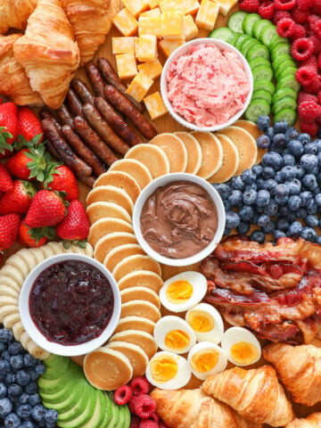 A Breakfast Charcuterie Board with spreads, pastries, fruits, eggs, bacon, and sausage.