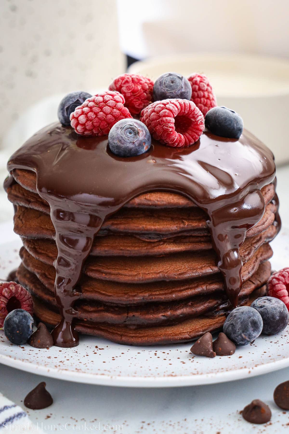 Stack of Chocolate Pancakes topped with chocolate ganache and berries.