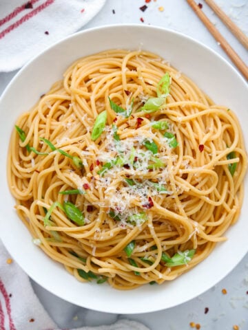 Plate of Garlic Noodles topped with parmesan cheese, green onions, and red pepper flakes.