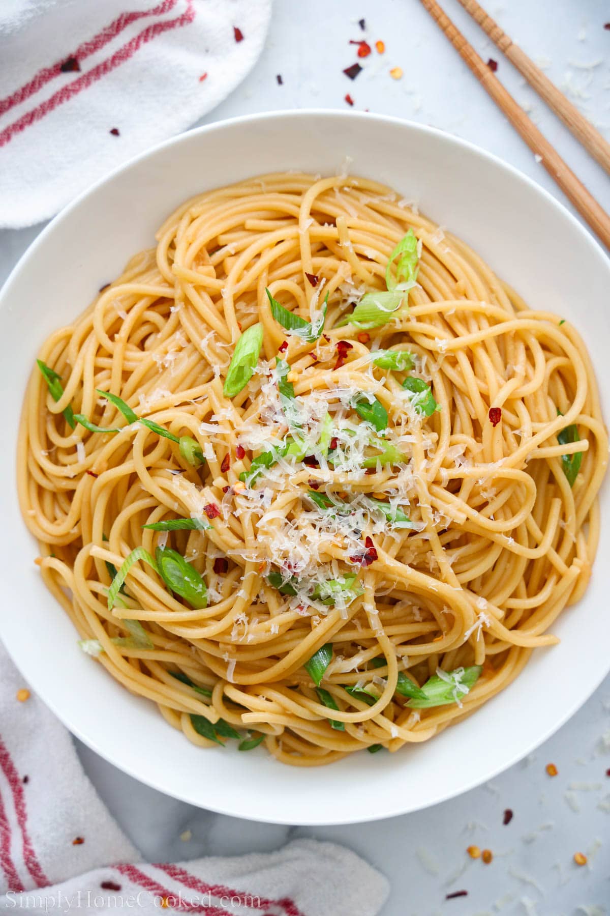 Plate of Garlic Noodles topped with parmesan cheese, green onions, and red pepper flakes.