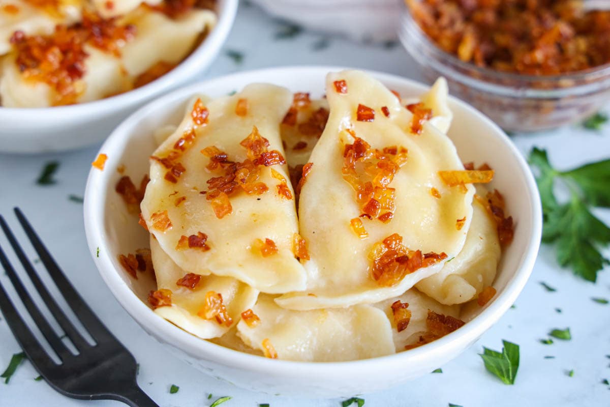 Potato Pierogi in a dish, covered with bacon bits and with a fork nearby.
