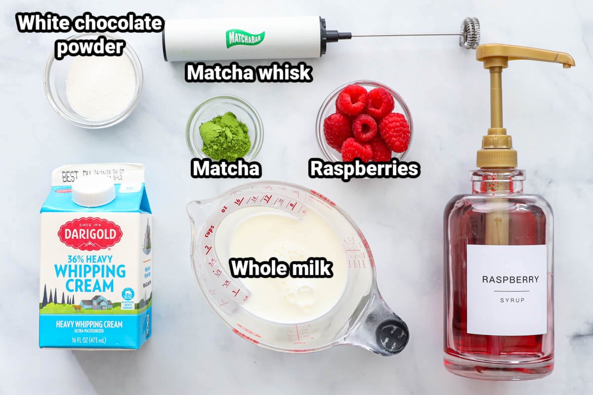 Ingredients for Raspberry Matcha Latte: white chocolate powder, heavy whipping cream, whole milk, raspberries, matcha, matcha whisk, and raspberry syrup.