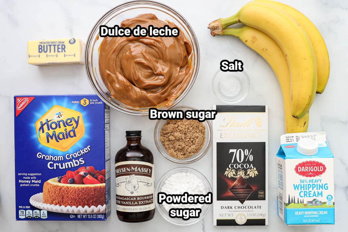 Ingredients for Banoffee Pie: graham cracker crumbs, butter, dulce de leche, salt, bananas, brown sugar, vanilla, powdered sugar, dark chocolate, and heavy cream.