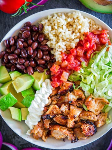 Close up of Chipotle Chicken Bowl with chicken, lettuce, salsa, rice, black beans, avocado, and sour cream.