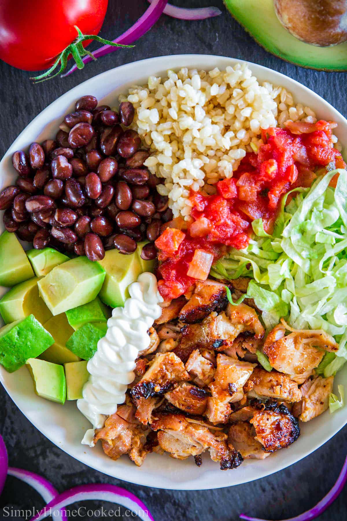 Close up of Chipotle Chicken Bowl with chicken, lettuce, salsa, rice, black beans, avocado, and sour cream.