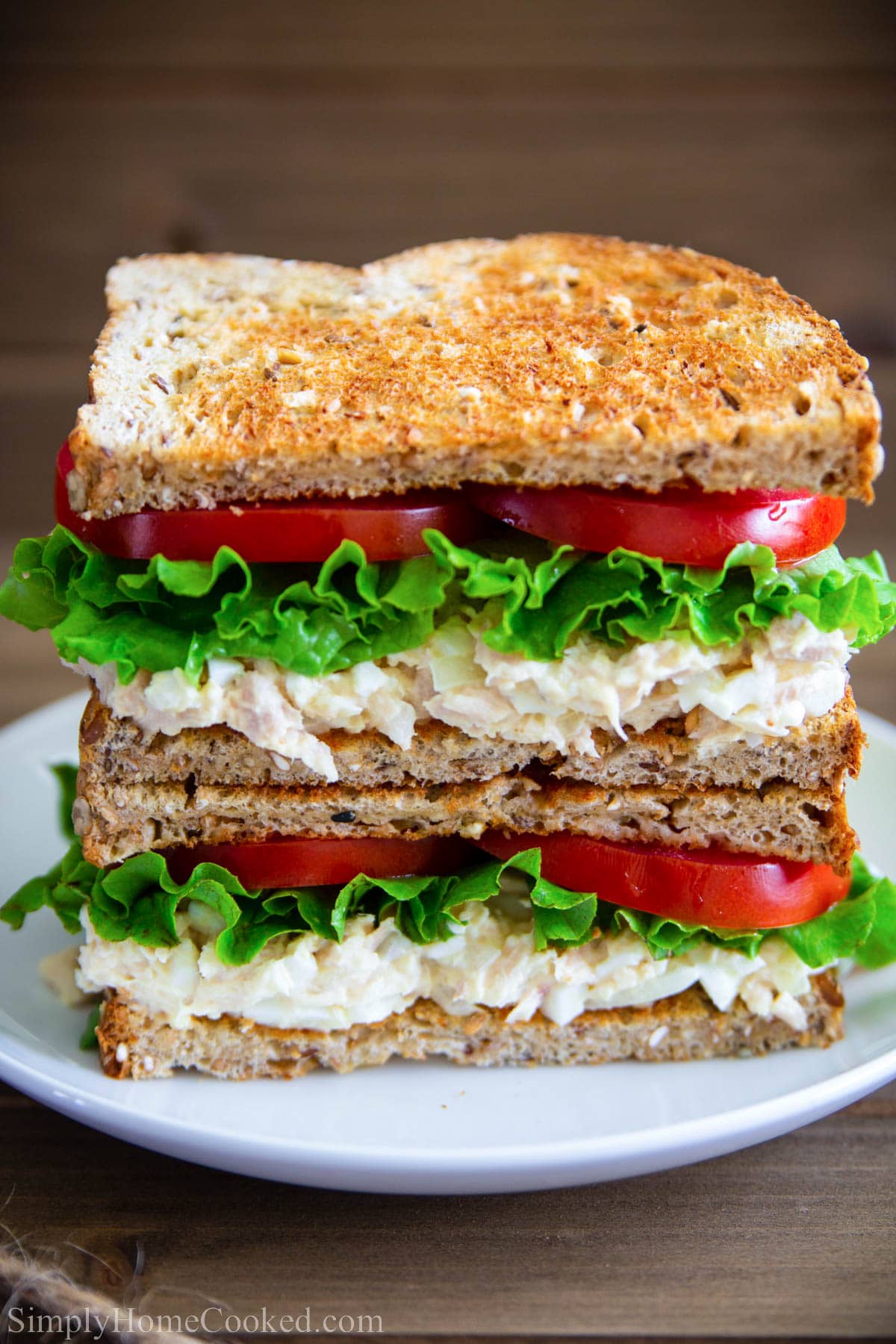 Tuna Salad Sandwich with tomato and lettuce cut in half and stacked.