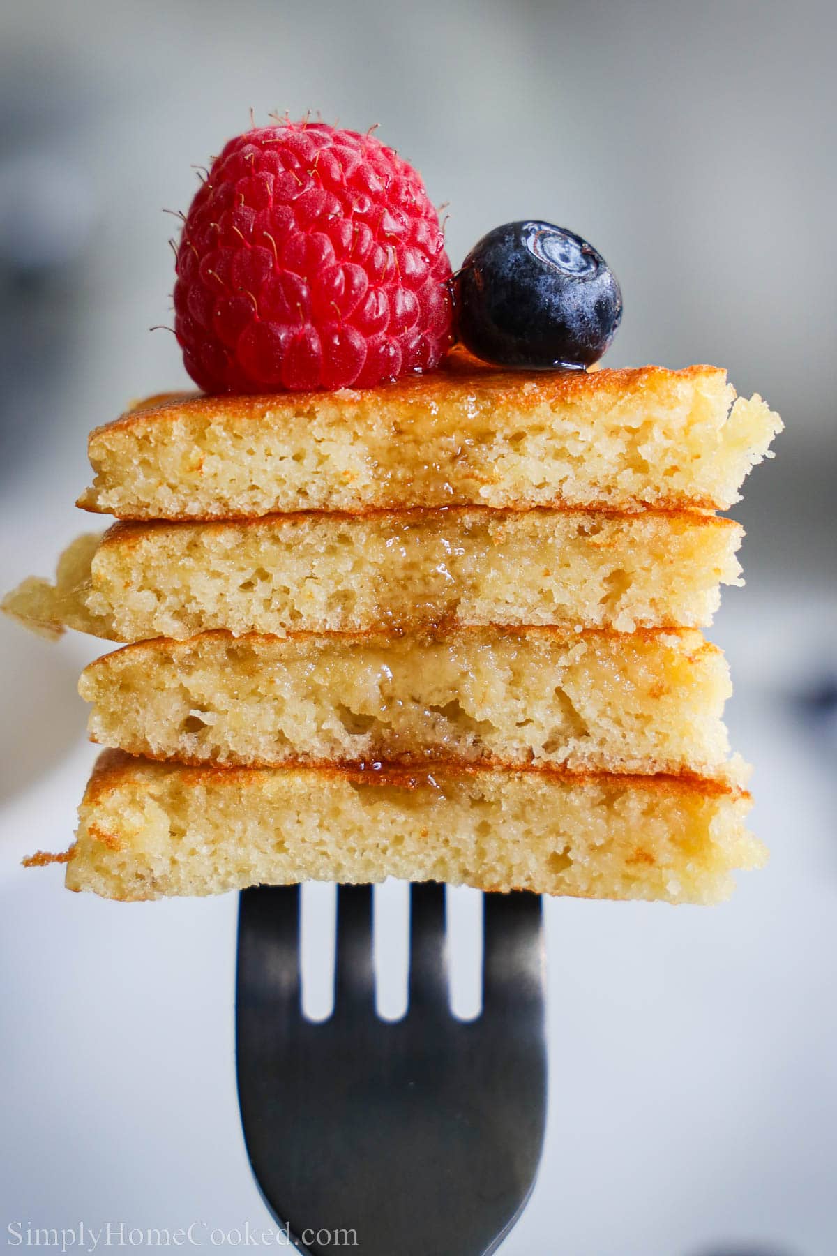 A fork with Almond Flour Pancakes on it with berries and syrup. 