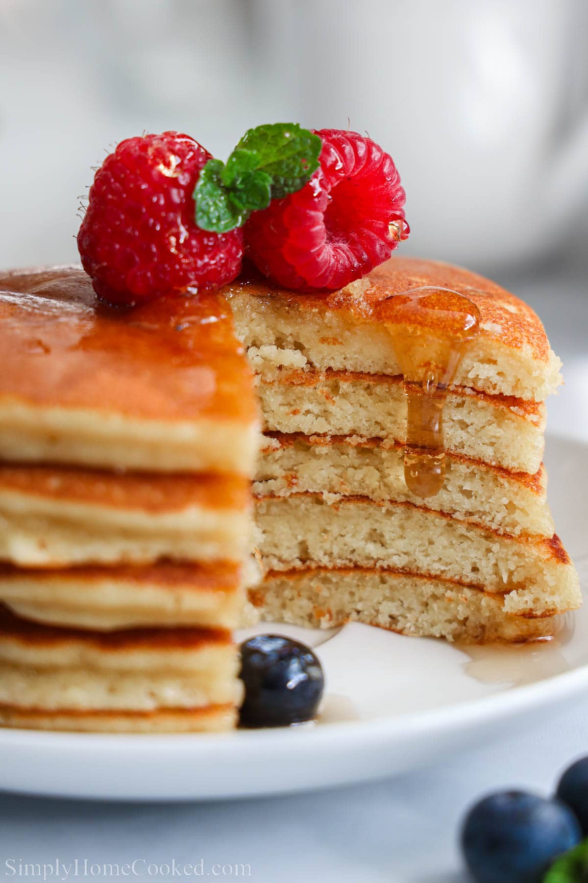 Close up of a stack of Almond Flour Pancakes missing a slice, topped with syrup and berries. 