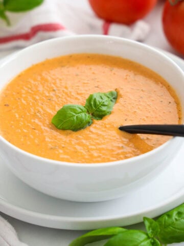 Bowl of Tomato Basil Soup topped with basil leaves and with a spoon inside.