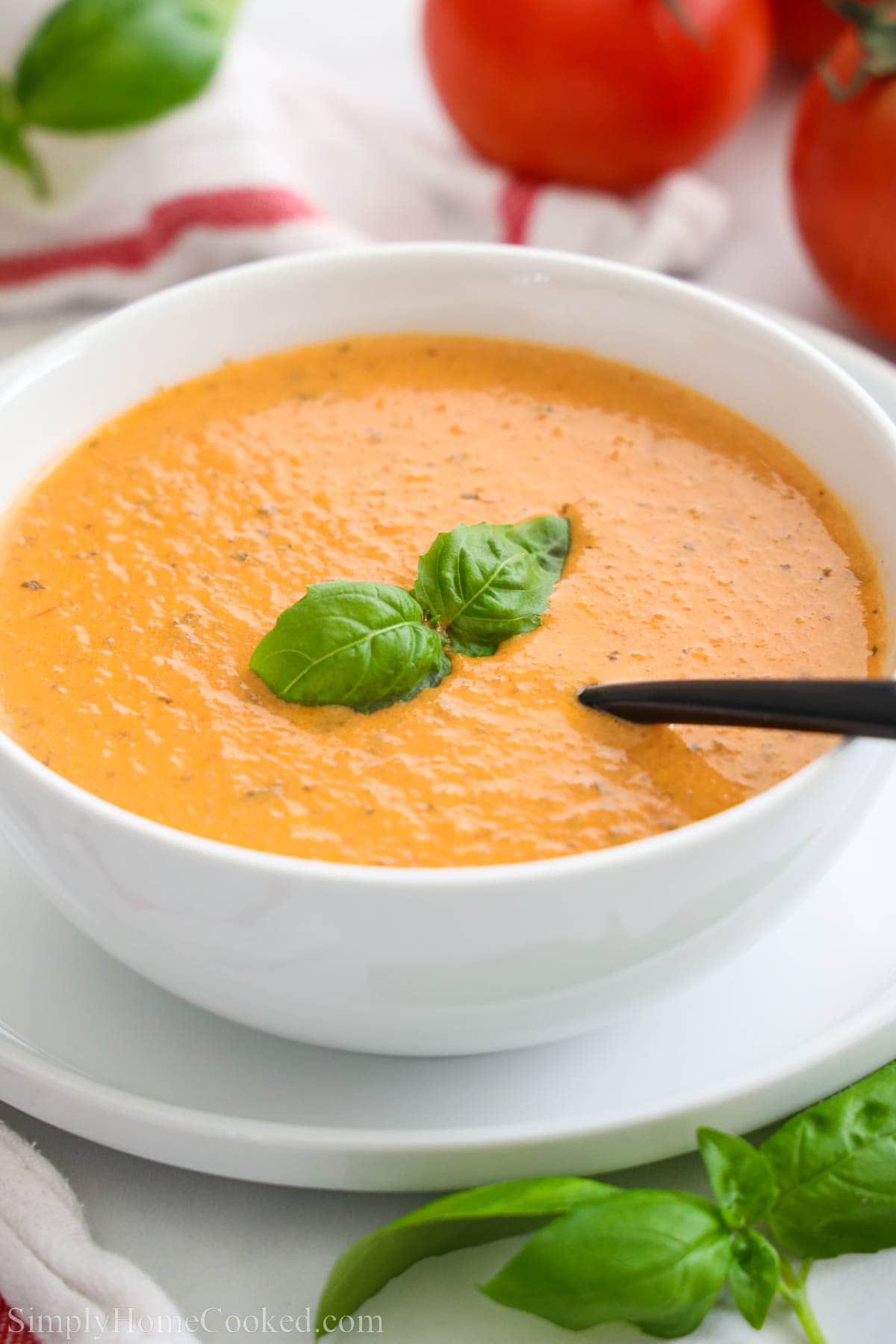 Bowl of Tomato Basil Soup topped with basil leaves and with a spoon inside. 