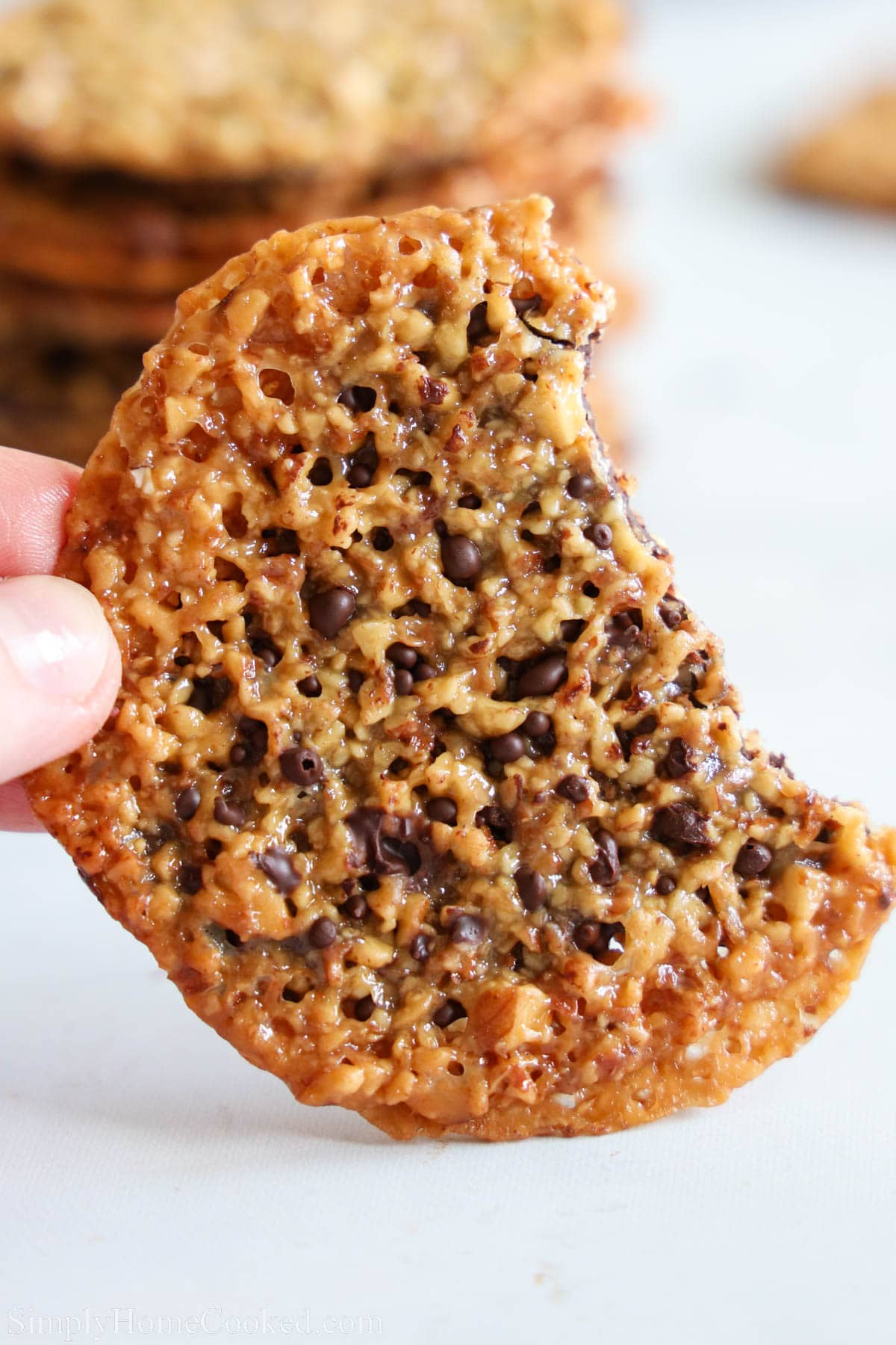 Close-up of Lace Cookie with Chocolate being held by fingers and missing a bite.