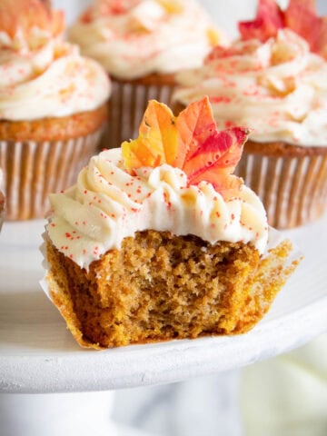 Pumpkin Spice Cupcakes with frosting and candy fall leaves, one missing a bite.