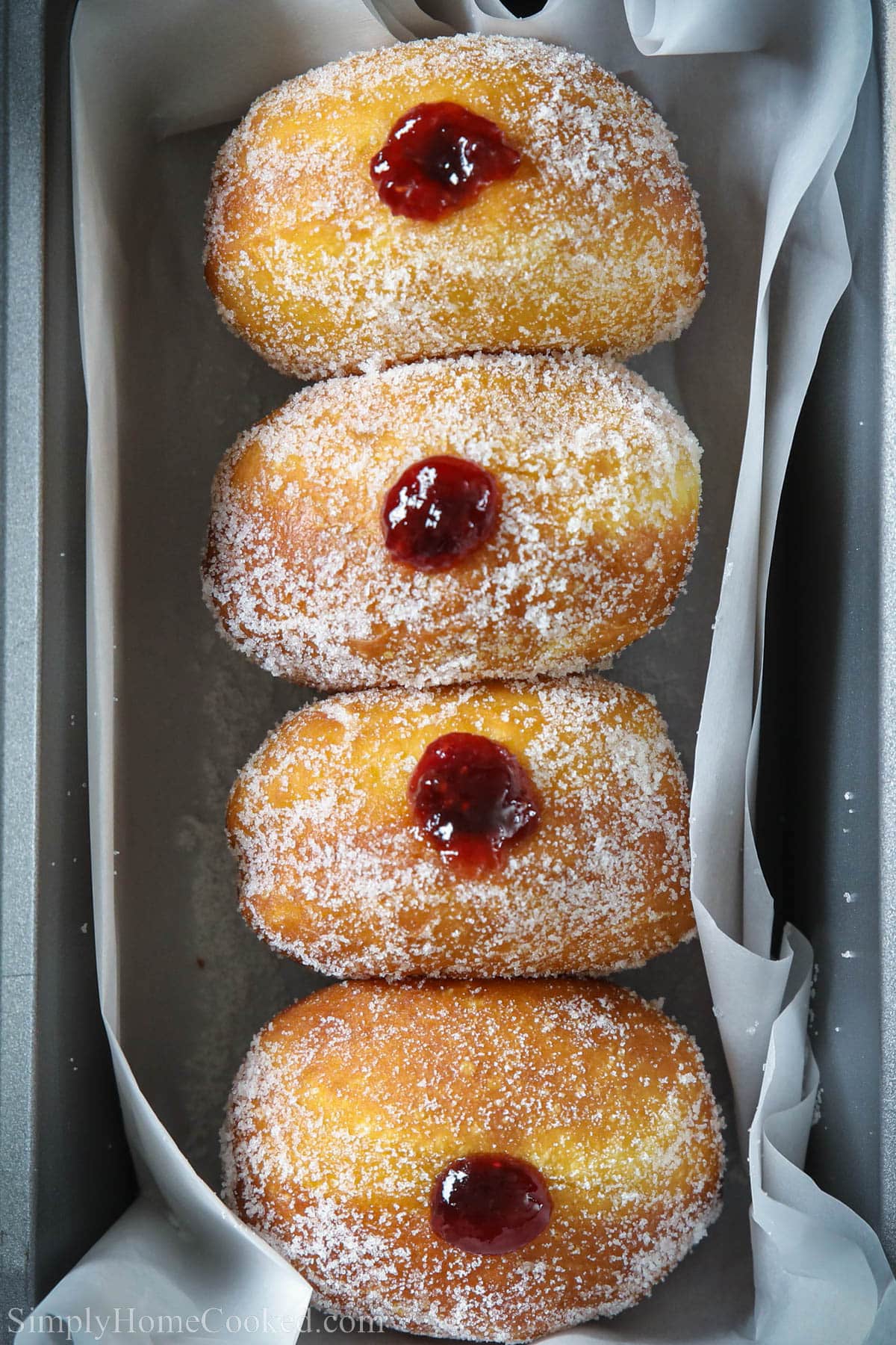 Brioche donuts in a pan, covered in sugar and with raspberry filling inside.