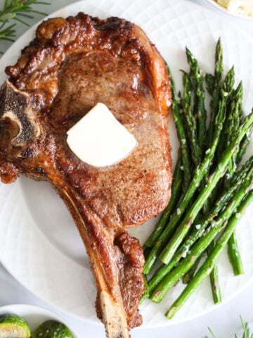 Ribeye Steak on a plate with asparagus and topped with butter.