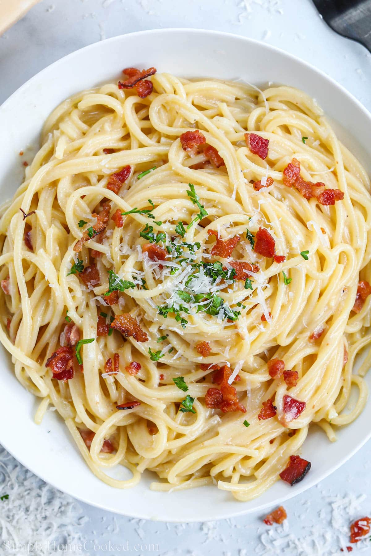 Overview of Spaghetti Carbonara topped with bacon, parmesan, and parsley.