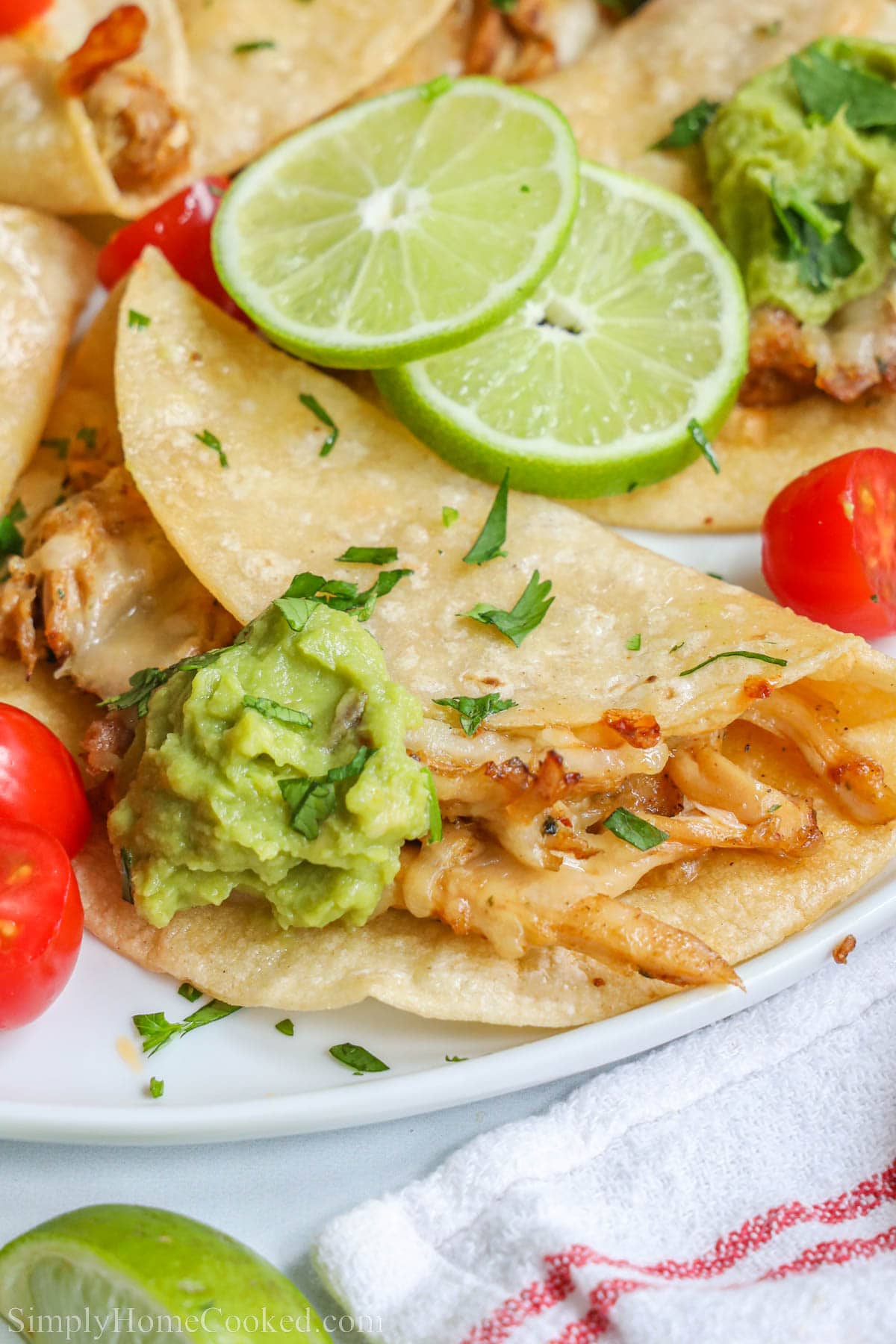 Close up of Baked Chicken Tacos, topped with lime, cilantro, and guacamole.