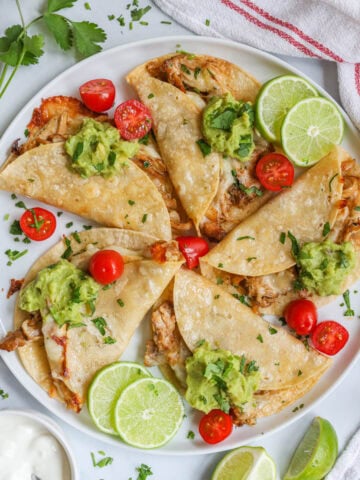 Baked Chicken Tacos topped with guacamole, lime slices, sliced cherry tomatoes, and chopped cilantro.