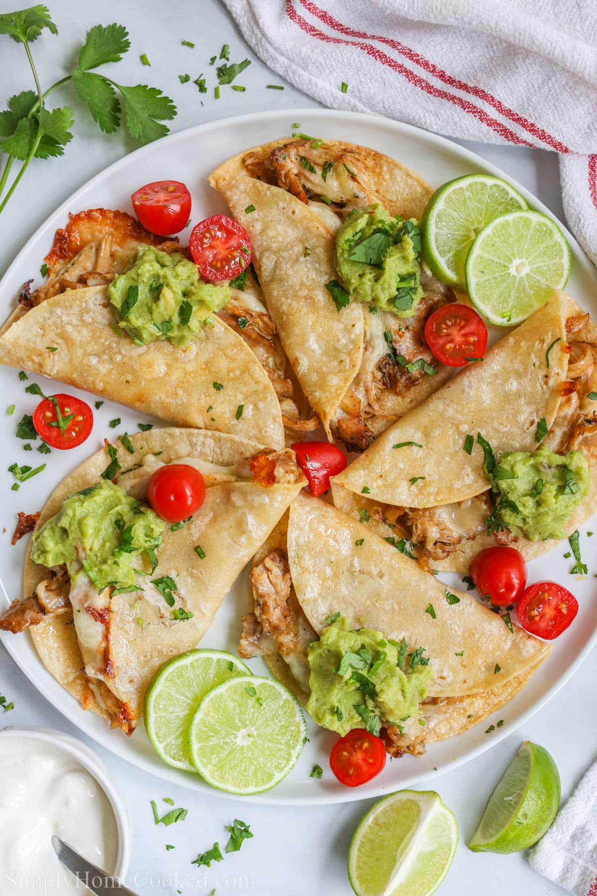 Baked Chicken Tacos topped with guacamole, lime slices, sliced cherry tomatoes, and chopped cilantro.
