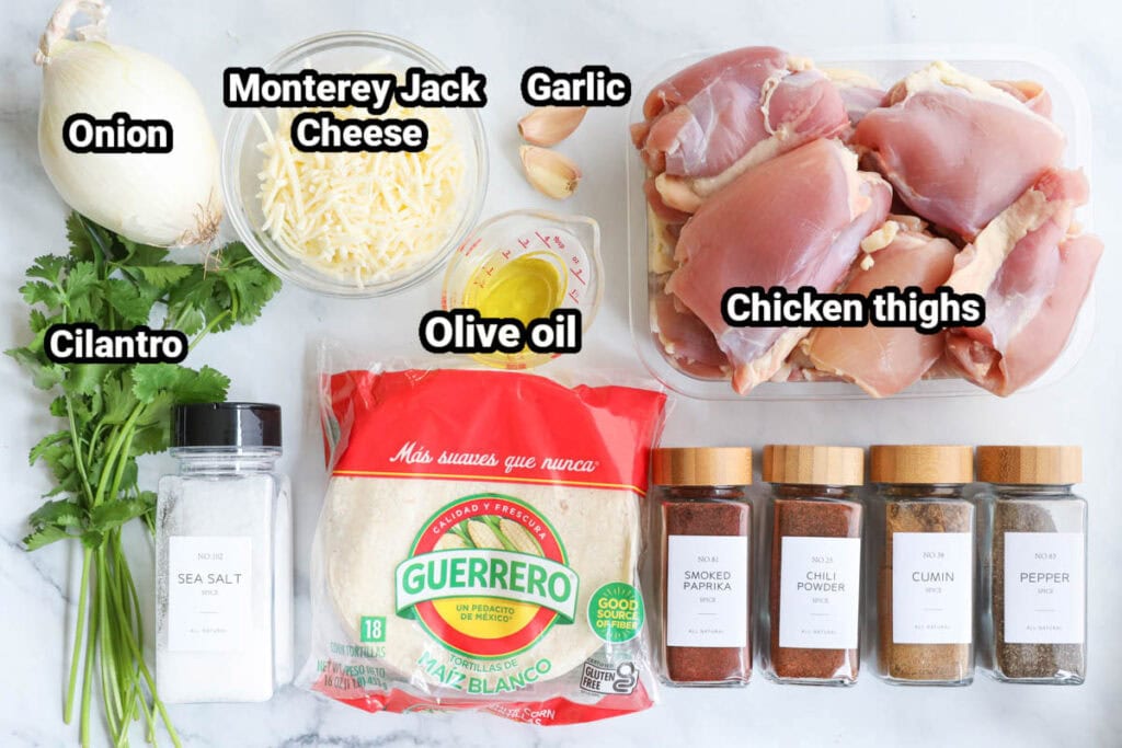 Baked Chicken Tacos ingredients: onion, Monterey jack cheese, garlic, olive oil, chicken thighs, cilantro, tortillas, sea salt, black pepper, smoked paprika, chili powder, and cumin.