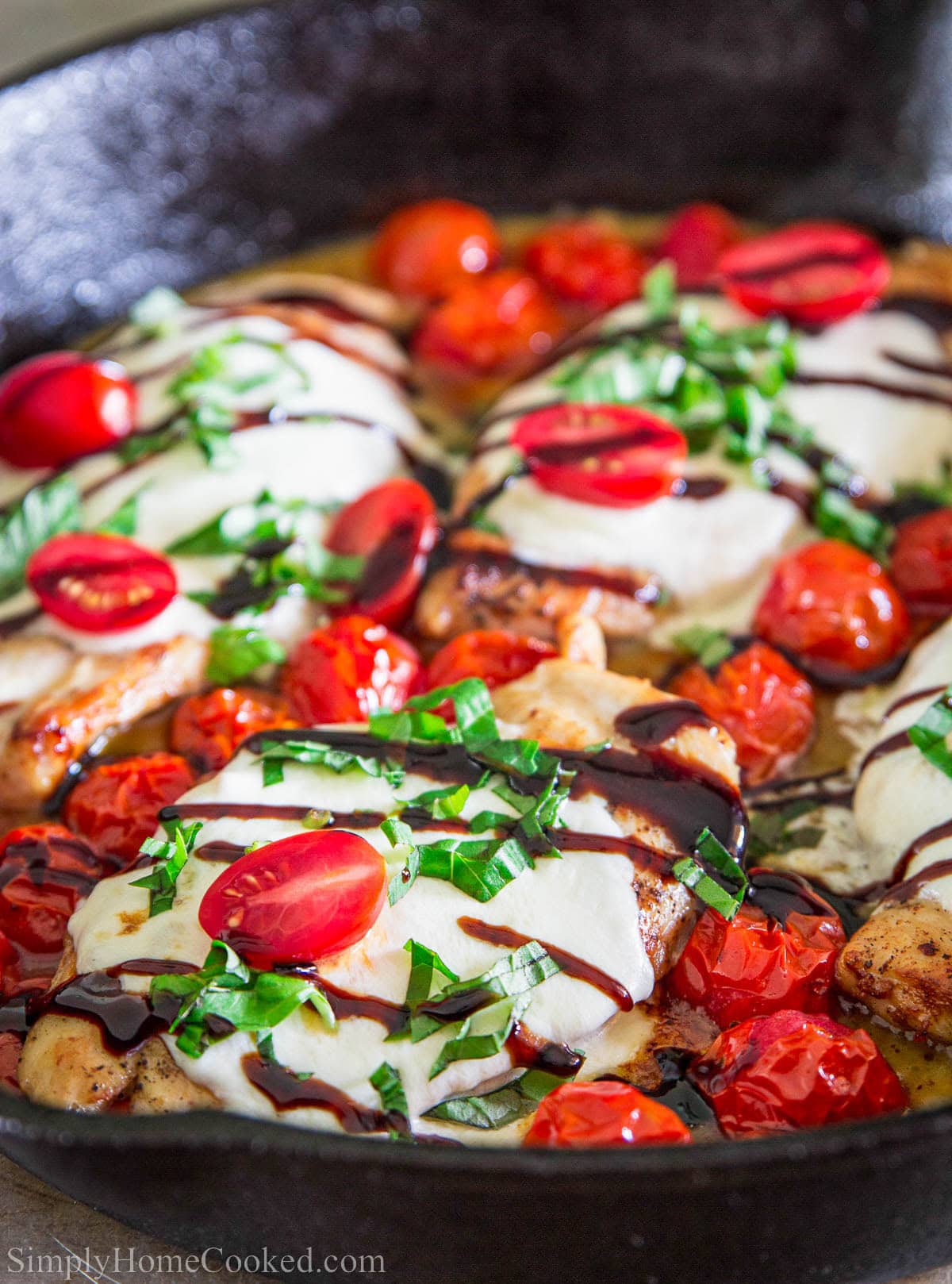Caprese Chicken in a skillet and topped with balsamic glaze and fresh basil.