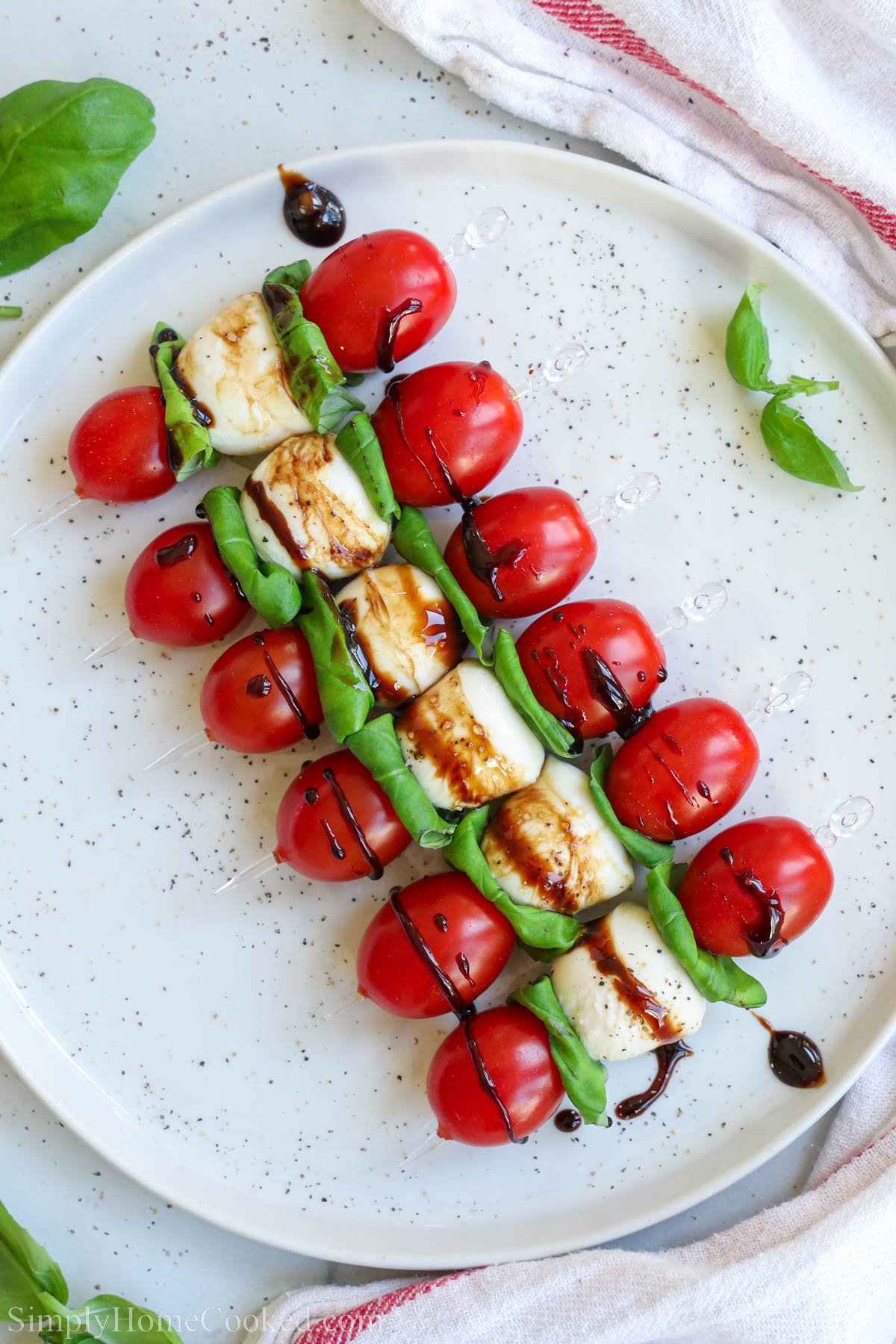 Caprese skewers lined up on the plate, drizzling down from the balsamic aze medicine.