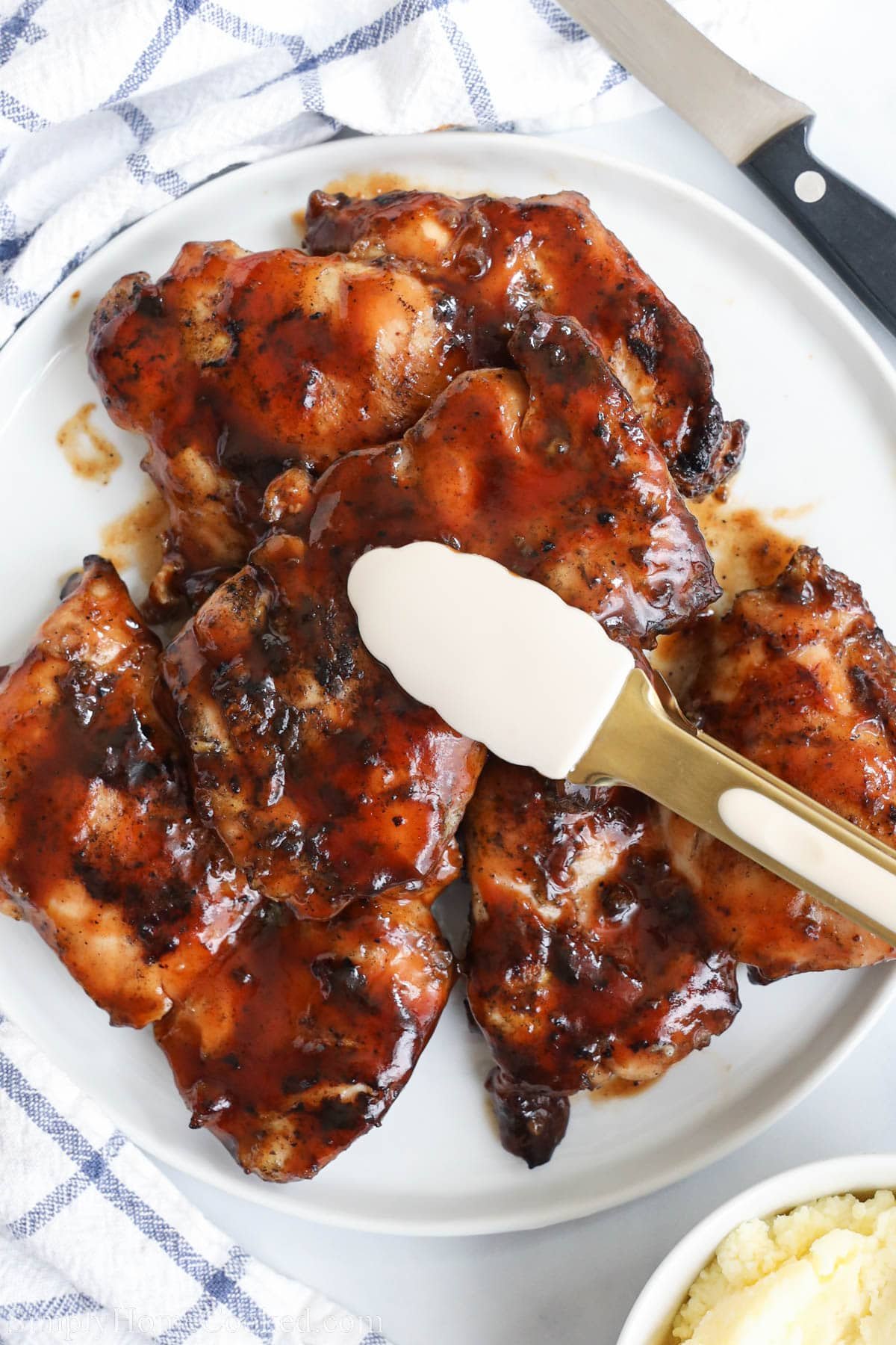 BBQ Chicken Thighs on a plate with tongs.