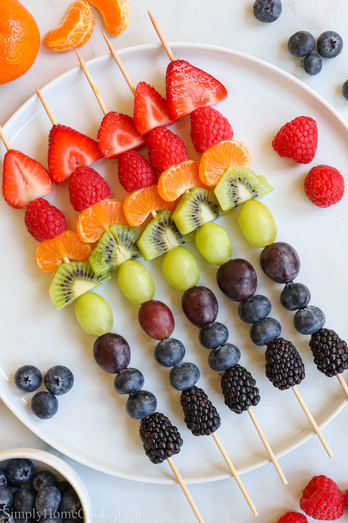 Fruit Kabobs lined up on a plate.