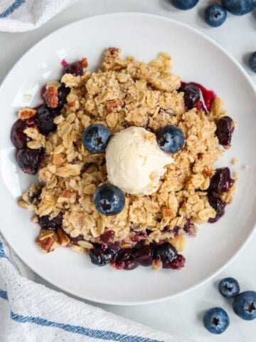 Overview of Blueberry Crisp topped with fresh blueberries and vanilla ice cream.