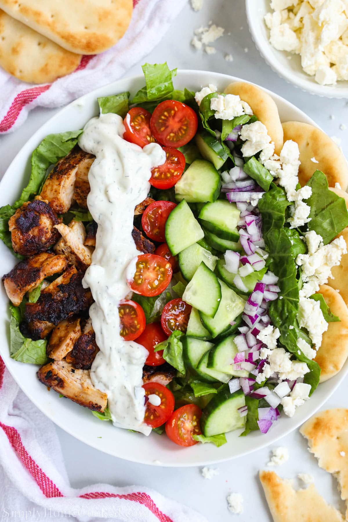 Overview of Chicken Shawarma Bowls, topped with tzatziki sauce, tomatoes, cucumbers, onion, feta cheese, and pita bread.