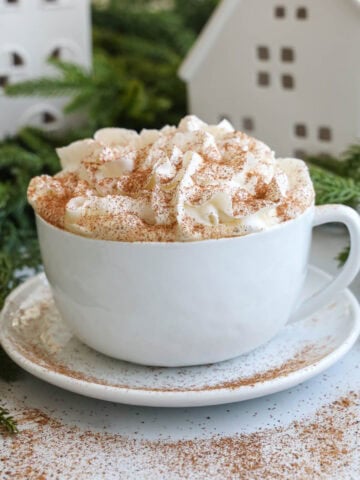 Eggnog Latte in a mug on a plate and topped with whipped cream and cinnamon,