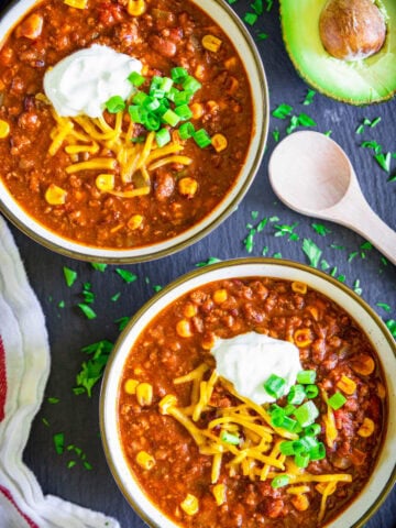 Easy Beef Chili in a bowl with cheese, green onions, and sour cream, and avocado on the side.