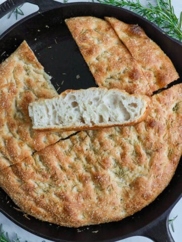 Sourdough Focaccia in a cast iron pan, cut, with one slice on top/