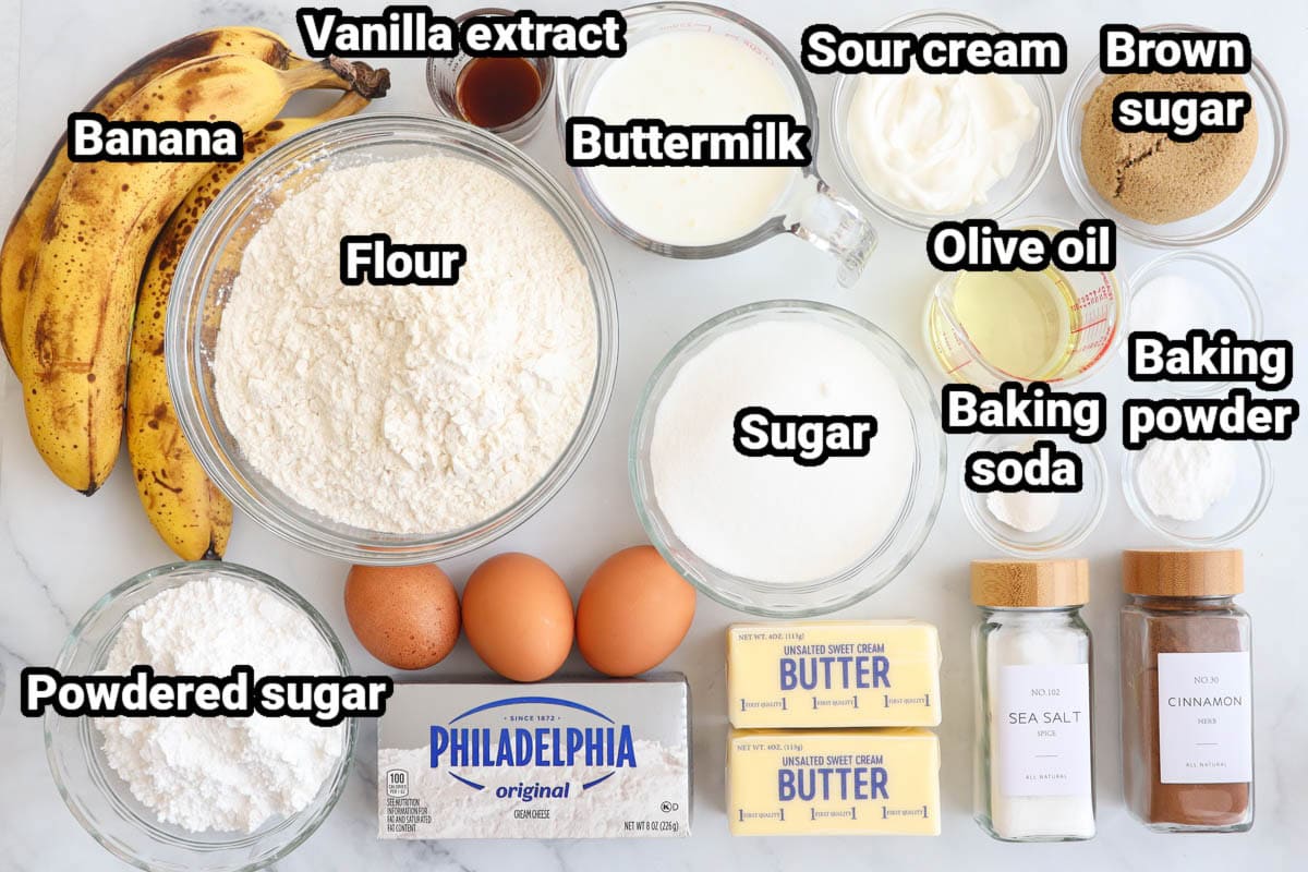 Ingredients for Banana Cake: flour, bananas, vanilla extract, buttermilk, sour cream, brown sugar, olive oil, sugar, baking soda, baking powder, eggs, powdered sugar, cream cheese, butter, salt, and cinnamon.
