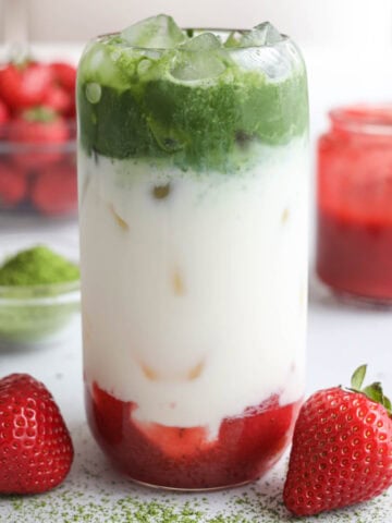 Close up of a Strawberry Matcha drink layered with matcha, milk, and strawberry puree, with a straw.