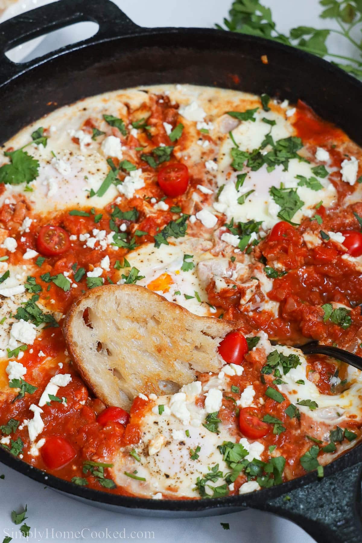 This Easy Shakshuka Recipe will really spice up breakfast. It's a unique spin on eggs that's easy to make and full of delicious spices and flavors. #shakshuka #shakshukarecipe #homemadeshakshuka #homemadeshakshukarecipe shakshuka in a cast iron pan with bread being dipped into it