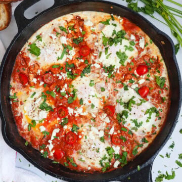 shakshuka in a cast iron pan with herbs and bread around
