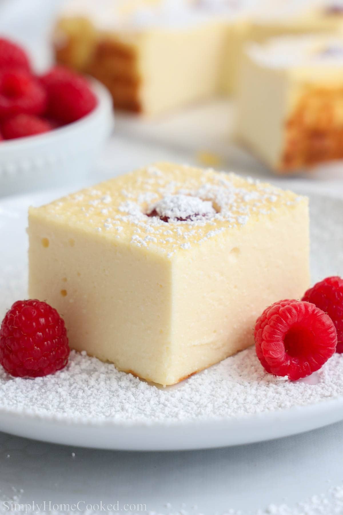 A slice of Zapekanka (Farmer's Cheese Cake) topped with powdered sugar and next to fresh raspberries.