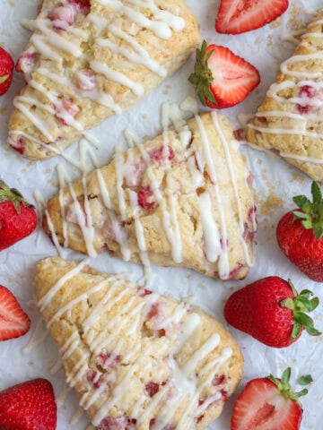 Strawberry Scones on parchment paper with strawberries and glaze drizzled on top.